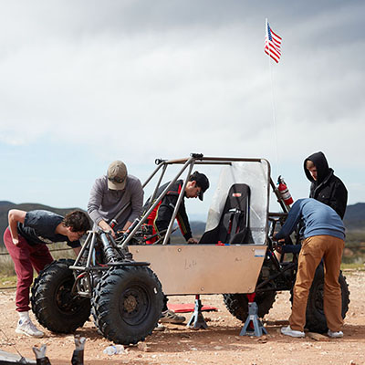 a team of male students working on a 4WD car out in the desert